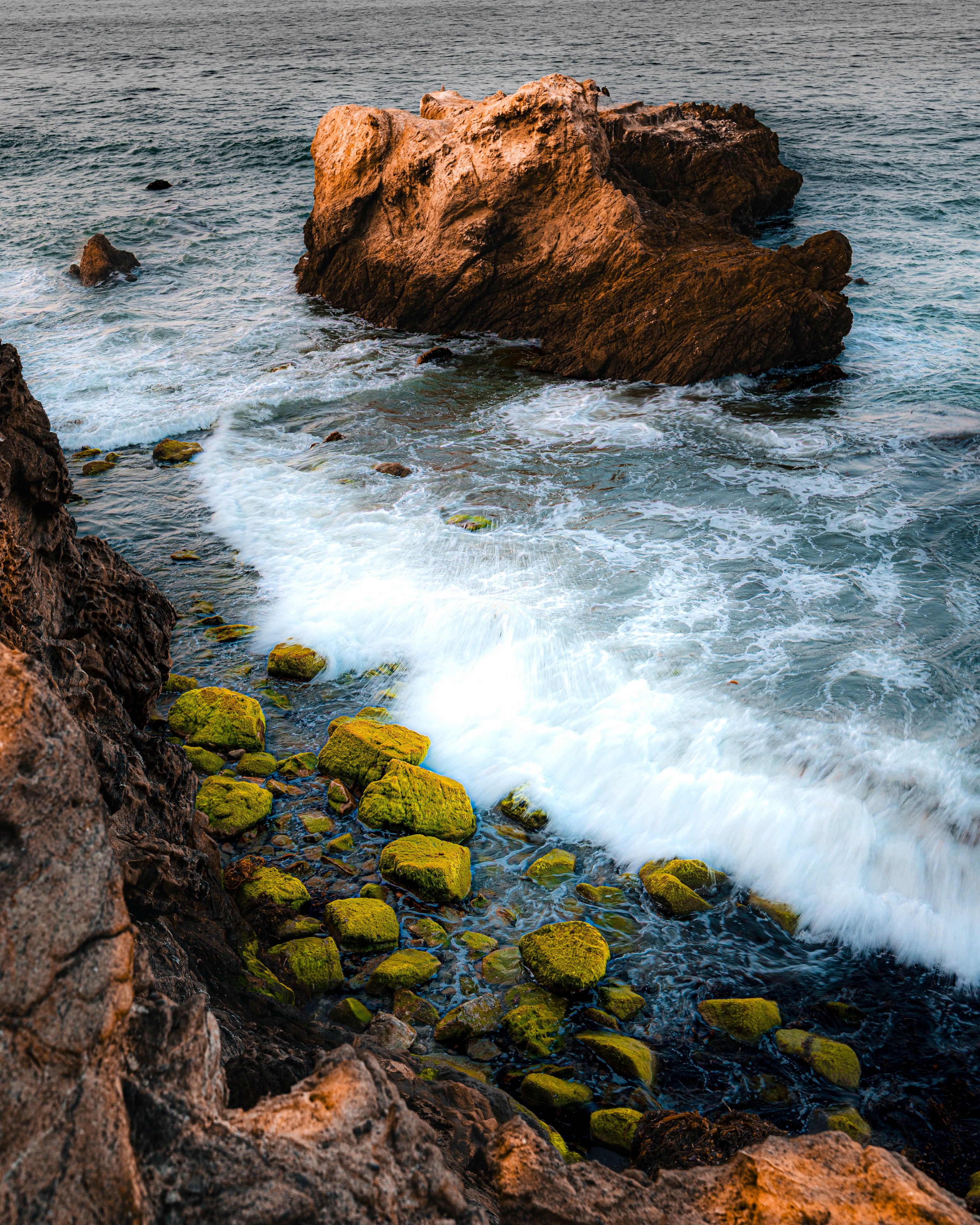 Moss-covered rocks and sea boulder with crashing waves
