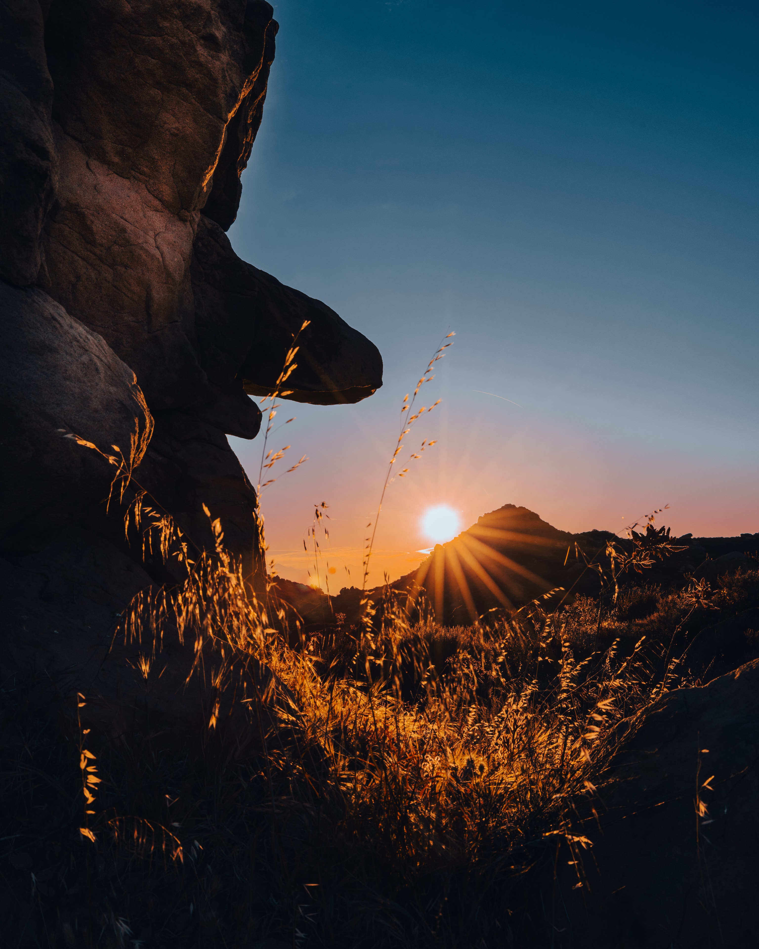 Sunburst over rocky terrain with golden grasses