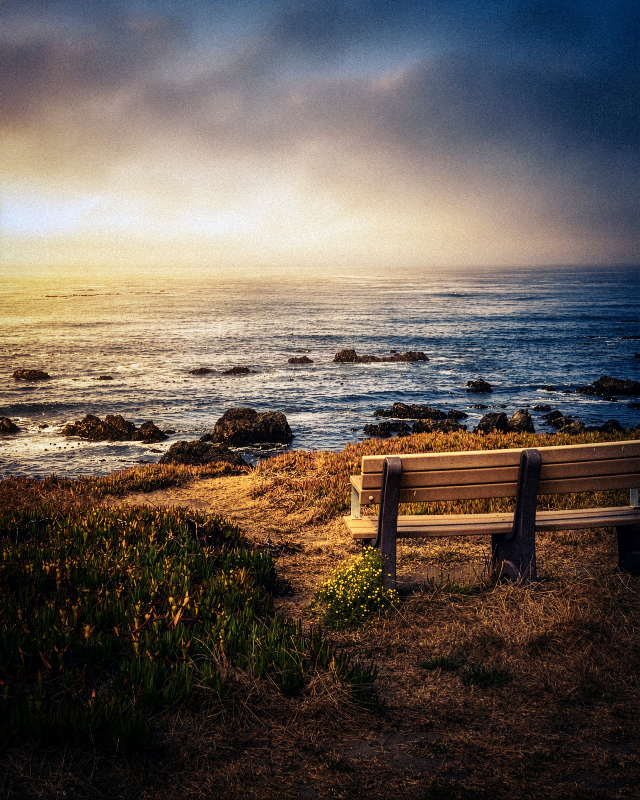 Coastal bench overlooking rocky shore at stormy sunset