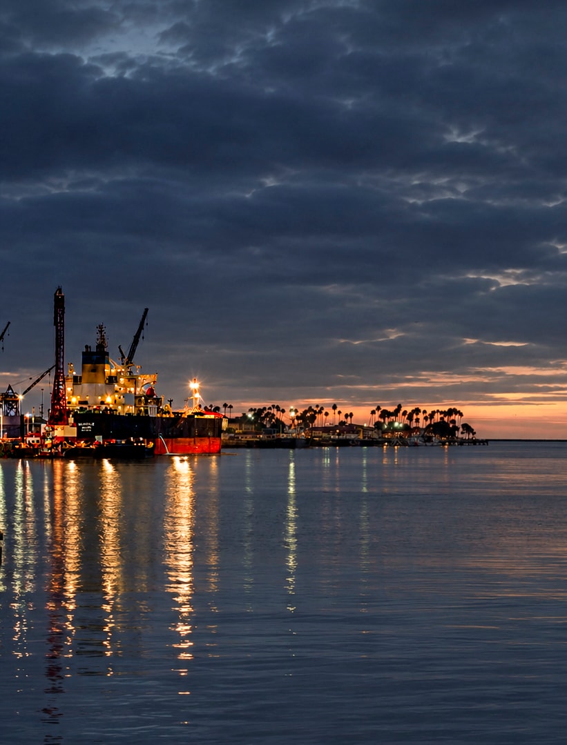 Industrial ship illuminated at dusk with calm harbor reflections