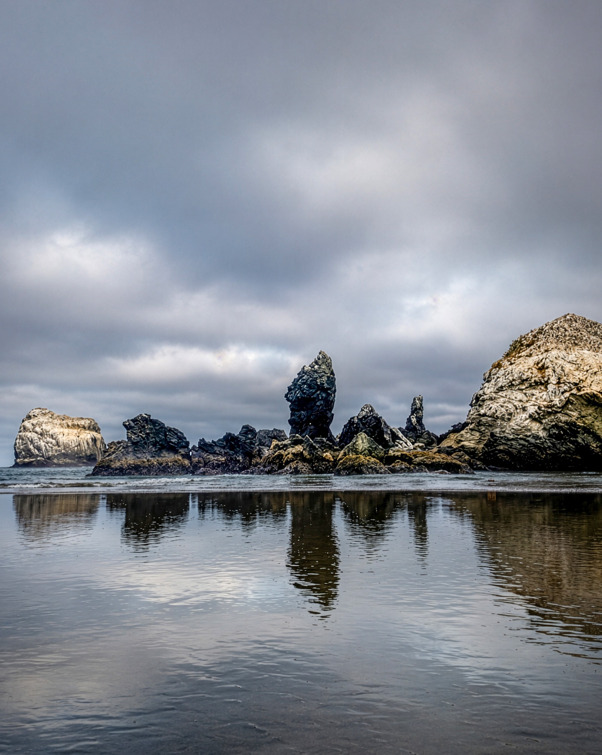 Jagged rock formations reflected in wet sand at low tide