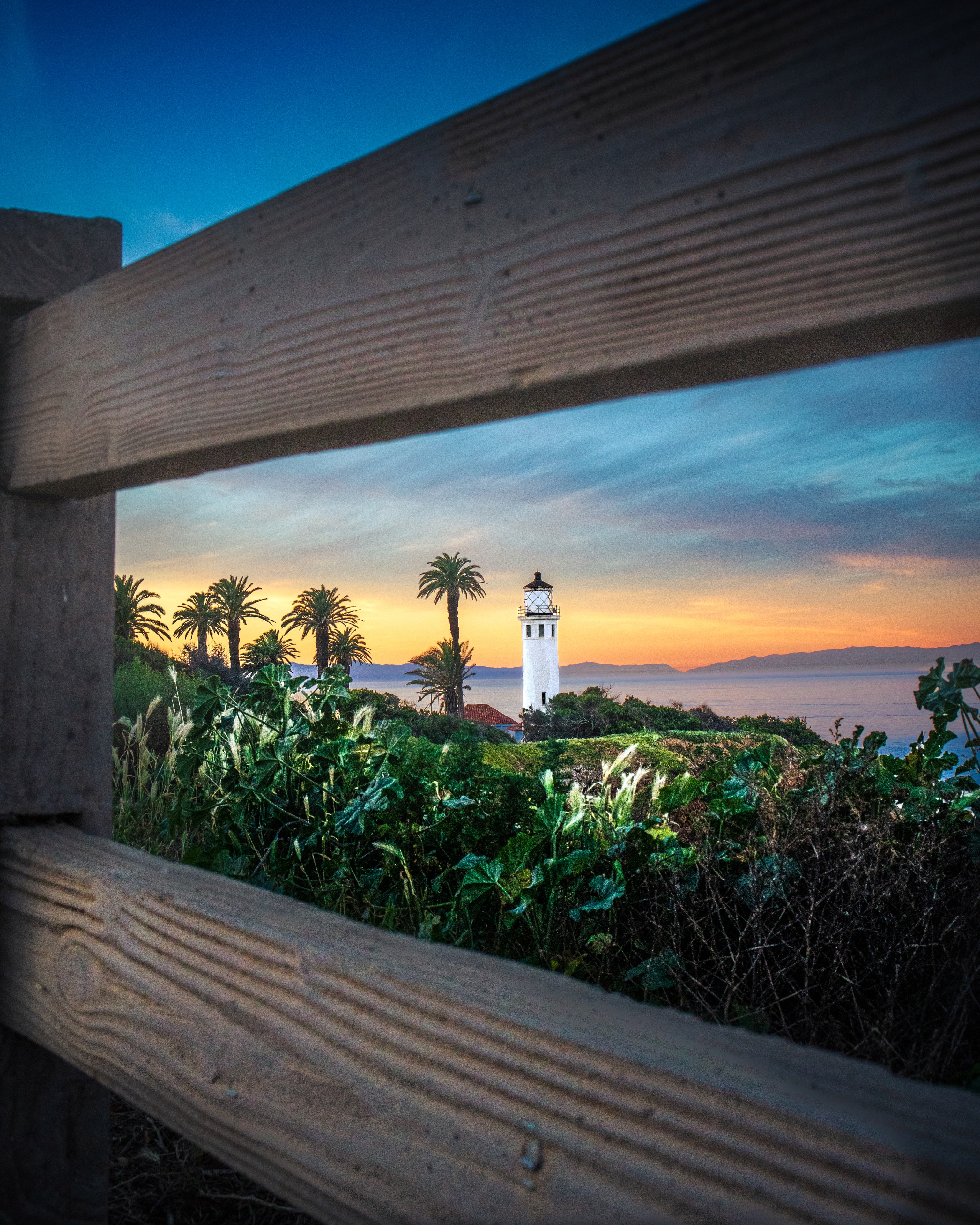 Lighthouse framed by wooden railing at vivid coastal sunset