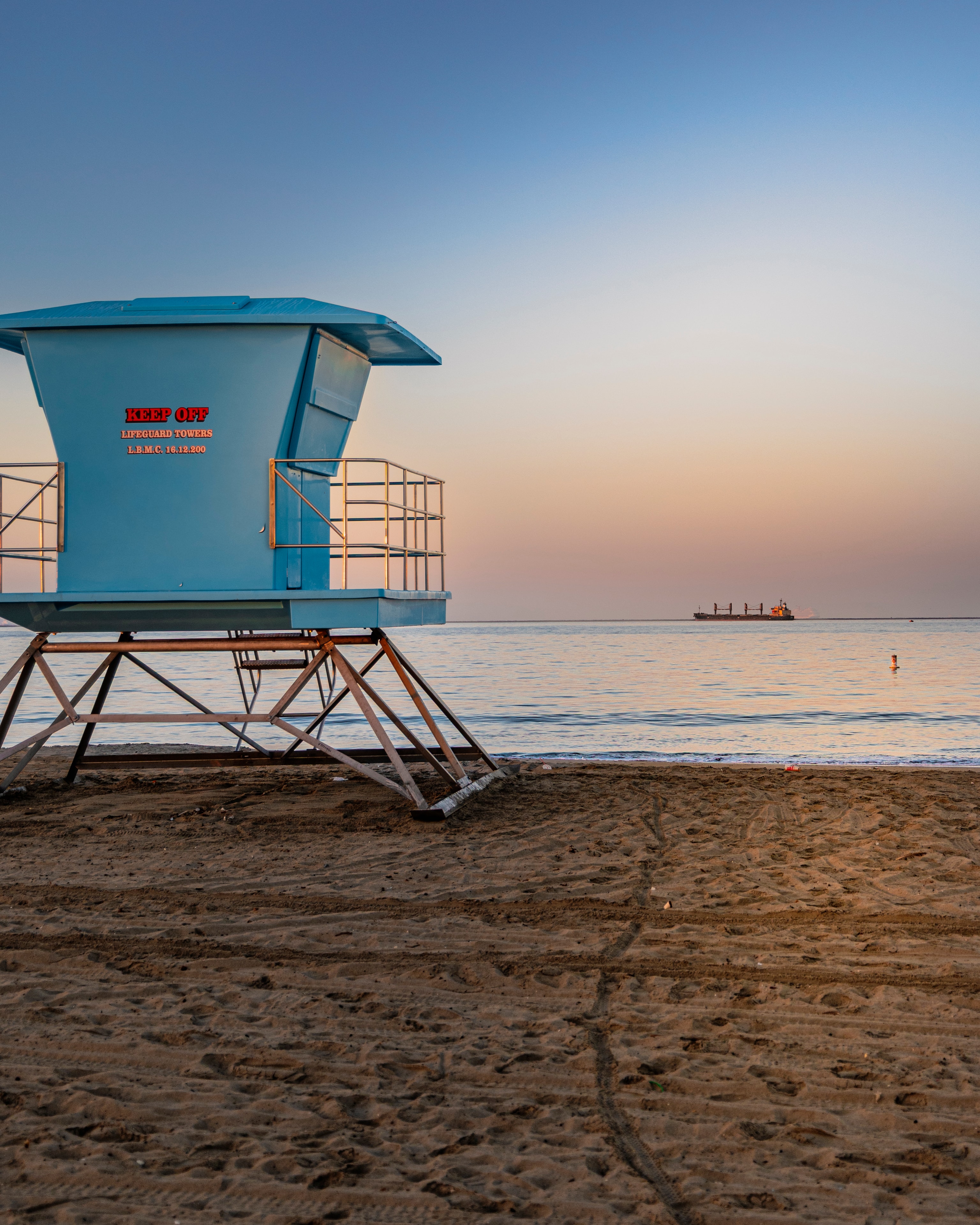 Blue lifeguard tower on sandy beach at sunset with cargo ship on horizon