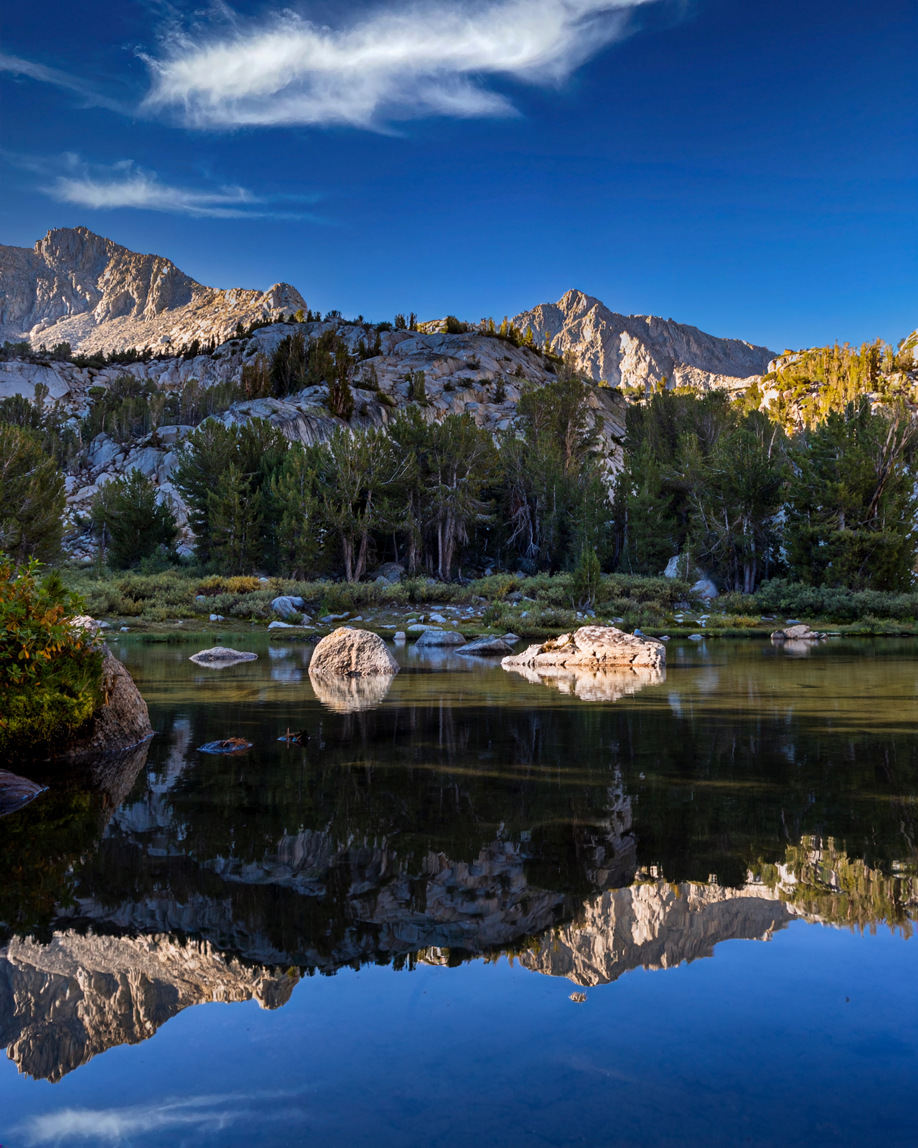 Granite peaks and pine forest perfectly reflected in calm alpine lake, Eastern Sierra